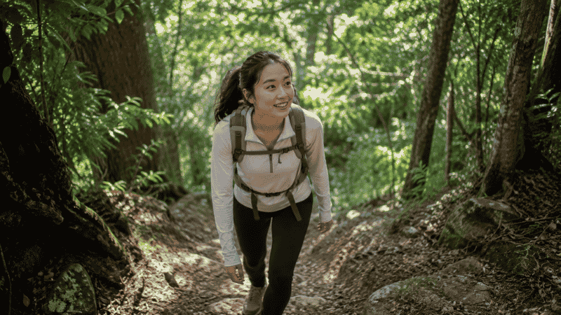 Beginner hiker climbing uphill on a forested trail, smiling despite the effort