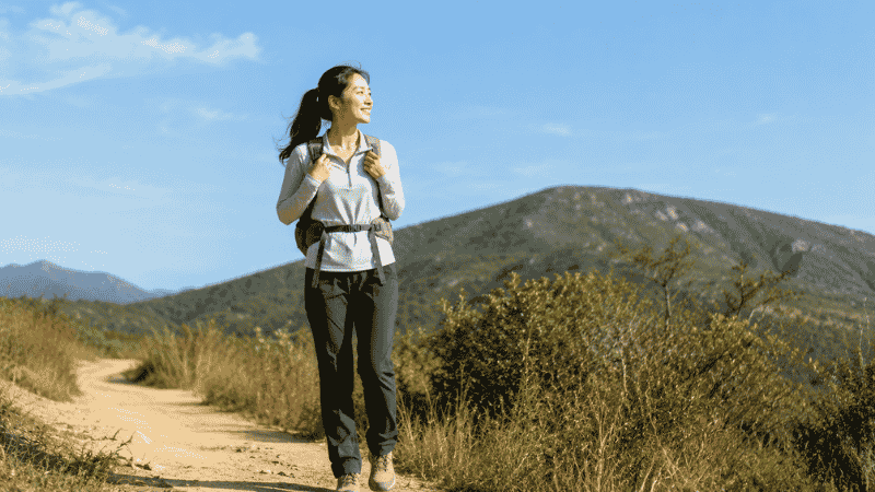 Young woman wearing a beginner hiking outfit including moisture-wicking top, quick-dry pants, trail shoes, and a daypack
