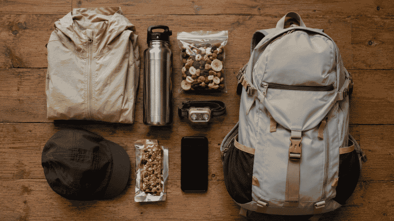 Hiking gear laid out on the floor the night before a beginner's first hike including daypack, water bottle, snacks, and headlamp