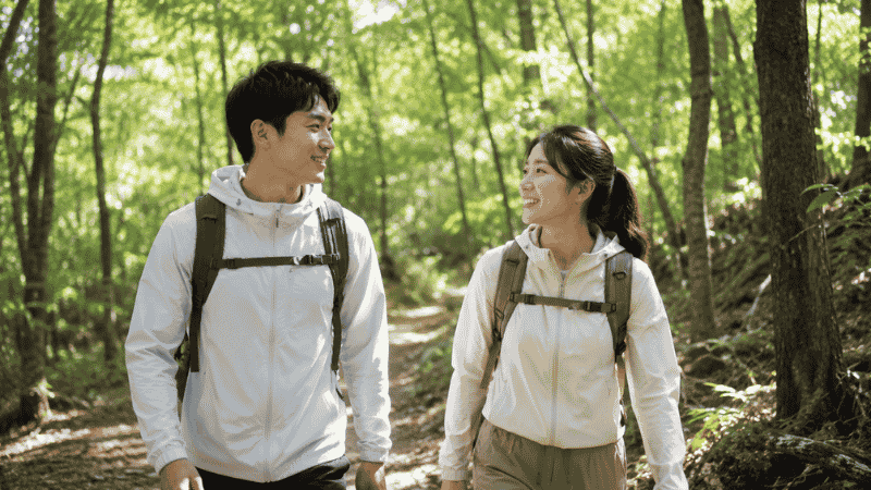 Two beginner hikers walking on a gentle forest trail with lightweight daypacks