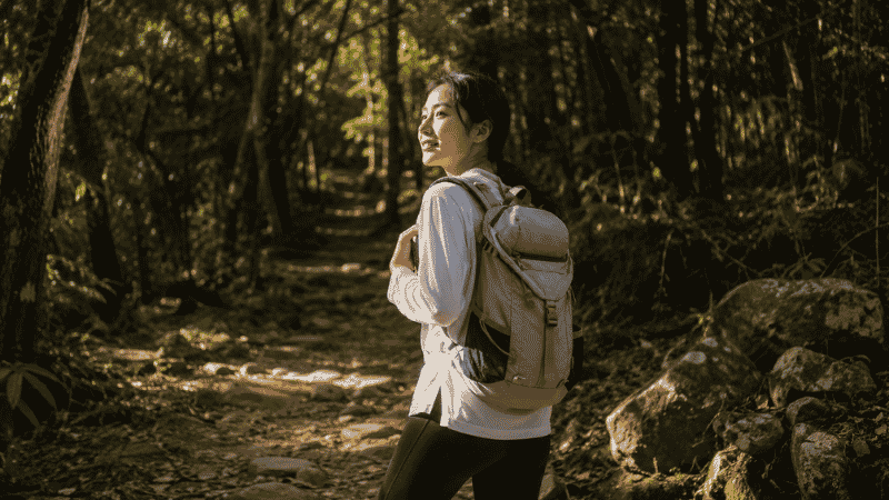 Young beginner hiker standing at the entrance of a forest trail with a daypack, ready for their first hike