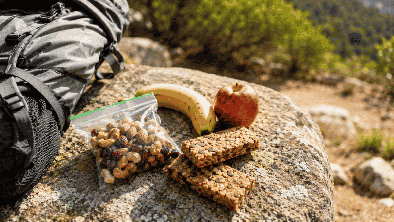 Trail snacks including trail mix, energy bars, and fruit laid out on a rock during a hiking break