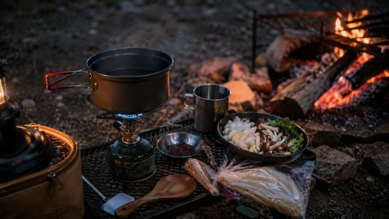 Camp stove with pot heating and camping cookware arranged at a campsite showing beginner-friendly camp cooking setup