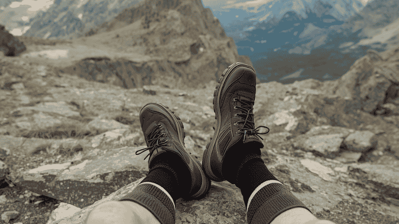 A hiker sitting on a granite rock with boots off, showing a pair of high-quality merino wool hiking socks against a scenic backdrop of rugged mountain peaks.