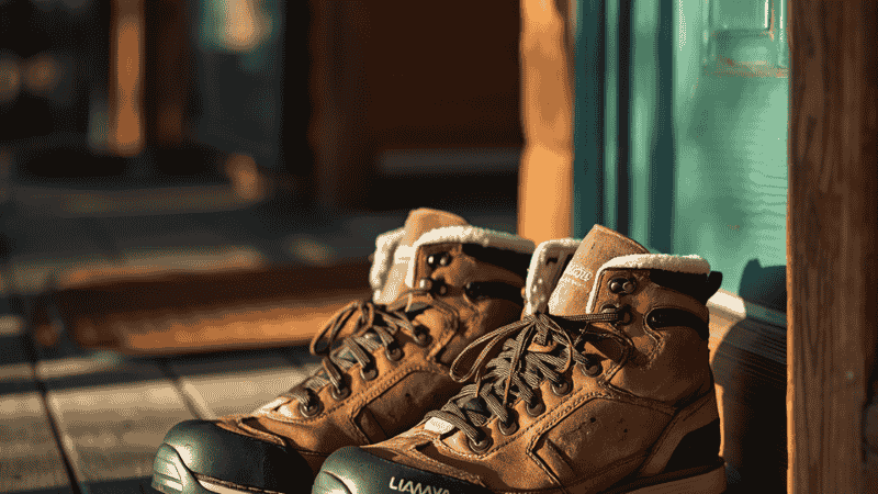 A pair of well-worn, mud-spattered leather hiking boots resting on a wooden porch after a successful summit hike, symbolizing durability and trail experience.