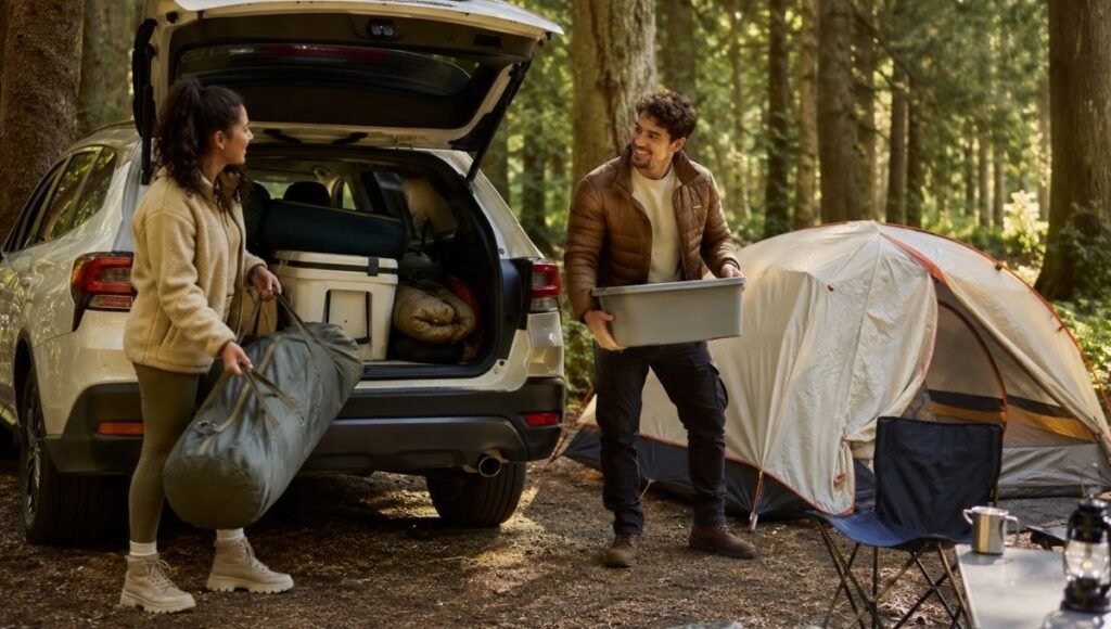Two young beginners unloading camping gear from an SUV at a forested campsite with a tent already pitched showing the ease and accessibility of car camping